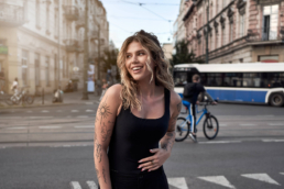 zdjęcie uśmiechniętej modelki w centrum miasta z rowerzystą i tramwajem w tle