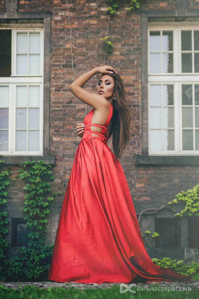 piękna kobieta w czerwonej sukni rozczesuje włosy pozując dla fotografa Dariusza Czepiela