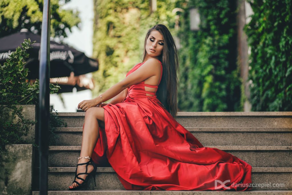 modelka w czerwonej sukni pozuje siedząc na schodach w zmysłowej pozie