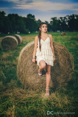dziewczyna w sukience opiera sie na beli siana podczas sesji fotograficznej w Krakowie