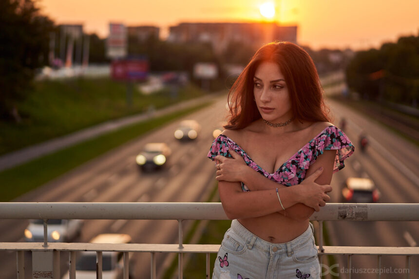 piękna brunetka pozująca na moście z samochodami w tle podczas sesji fotograficznej Dariusza Czepiela w Krakowie